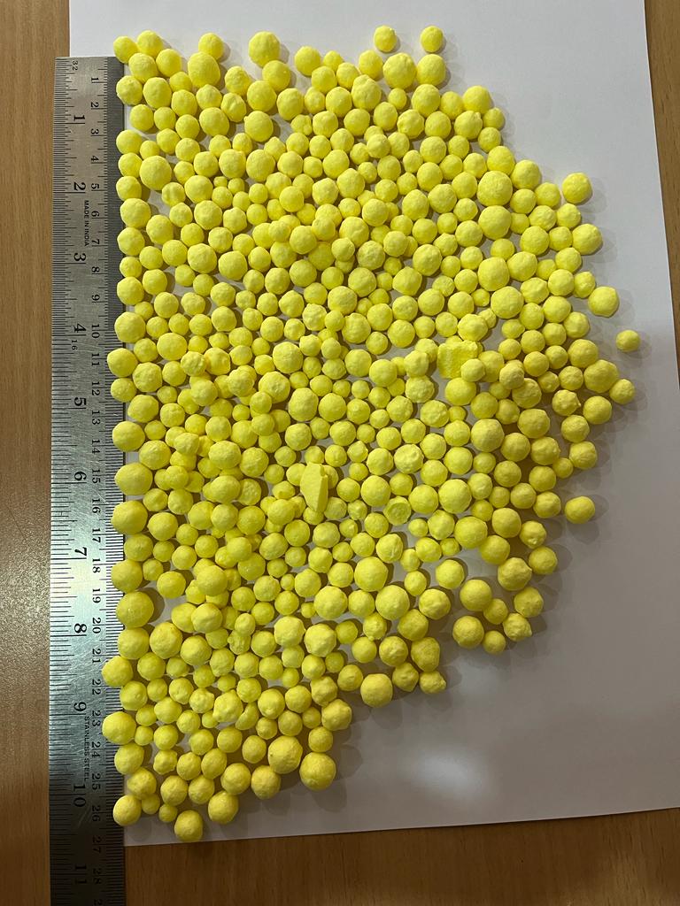 Bright yellow sulphur granules measured against a steel ruler
